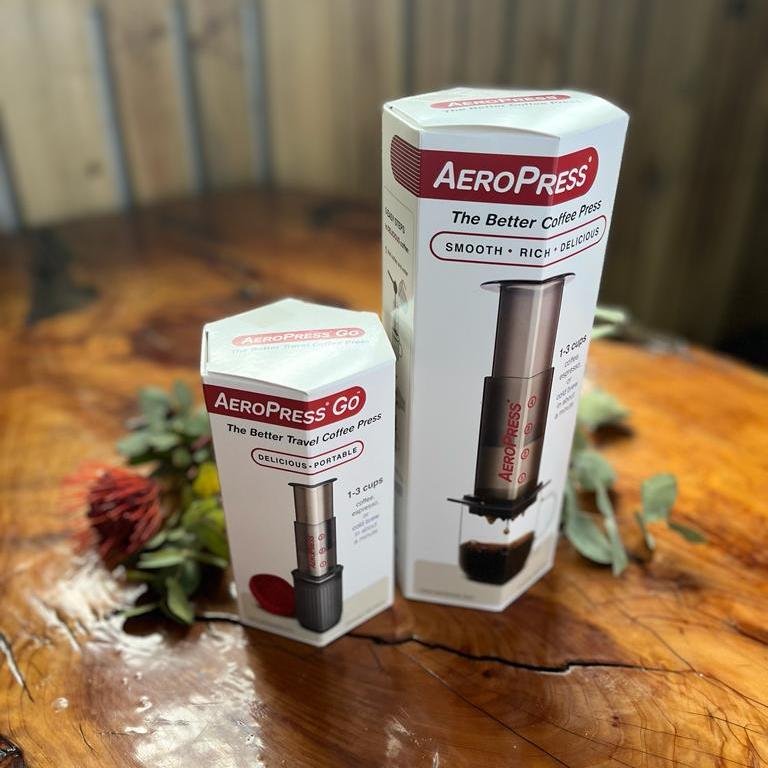 Aeropress original and aeropress go sitting on timber table beside a flower