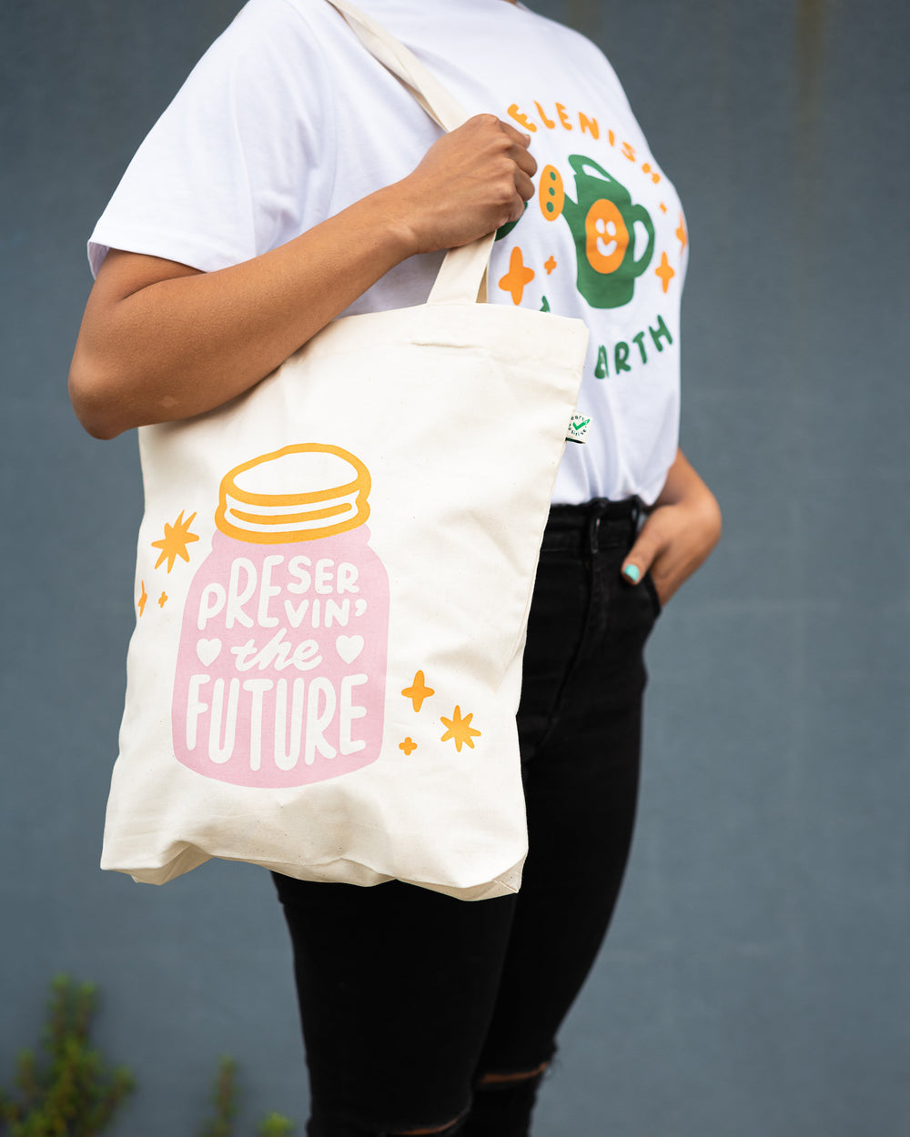 arm holding organic white cotton tote with pink and orange design showing a jar with words preserving the future inside