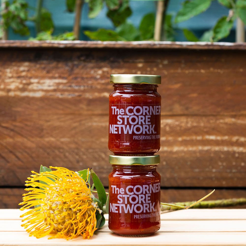 two jars of chilli jam made from donated chillies stacked on timber box next to flower