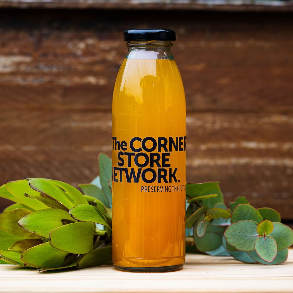 bottle of orange cordial made from donated oranges on timber box next to flower