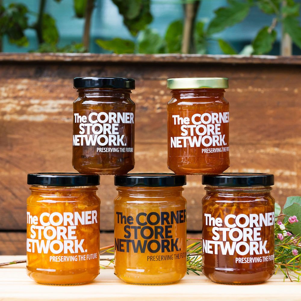 five jars of marmalade stacked in a pyramid in front of a veggie planter