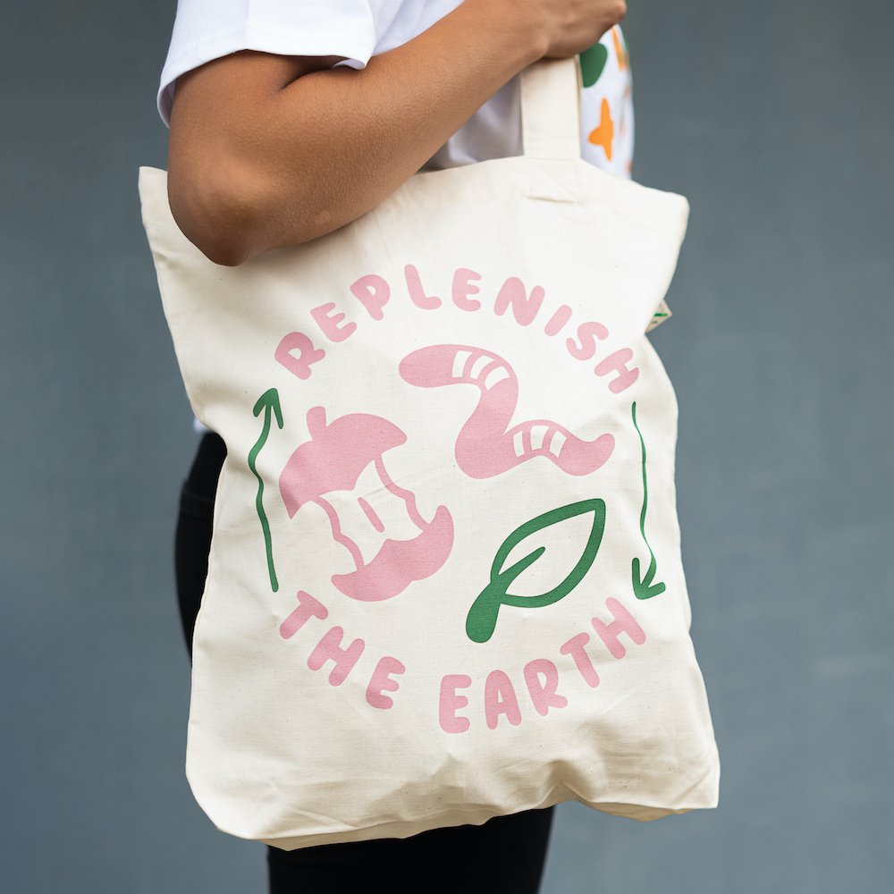 organic white cotton tote with pink and green design saying replenish the earth with apple, worm and leaf
