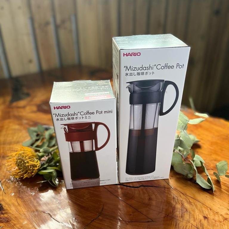 a 600ml and 1 litre Hario 'Mizudashi' Cold Brew Pot sat beside each other on a timber table beside a flower