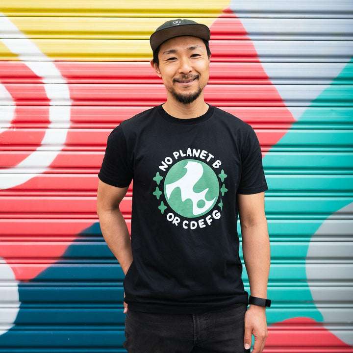 smiling man in front of colourful wall wearing black organic cotton shirt with blue and green design saying no planet b or cdefg surrounding planet earth