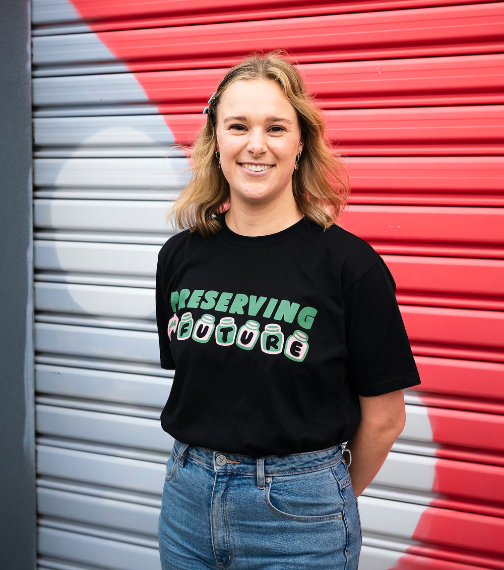 smiling woman in front of colourful wall wearing black organic cotton shirt saying preserving the future