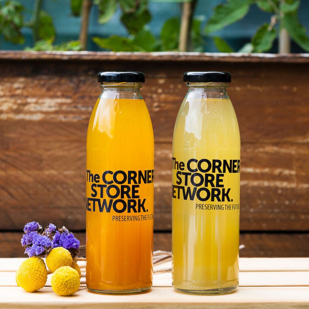 two bottles of cordial made from donated citrus on timber box next to flowers