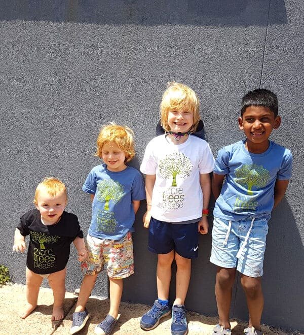 four children wearing tees with an illustrated tree and the words more trees please underneath, in various colours