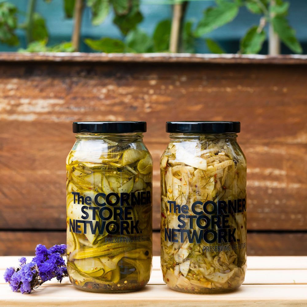two large jars of pickles made from donated cucumbers on timber box next to flower