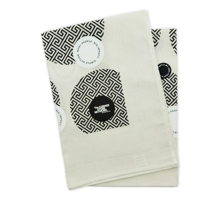 white linen tea towel folded, featuring black and white patterned circles amongst other circles housing the worlds simple action many people big impact