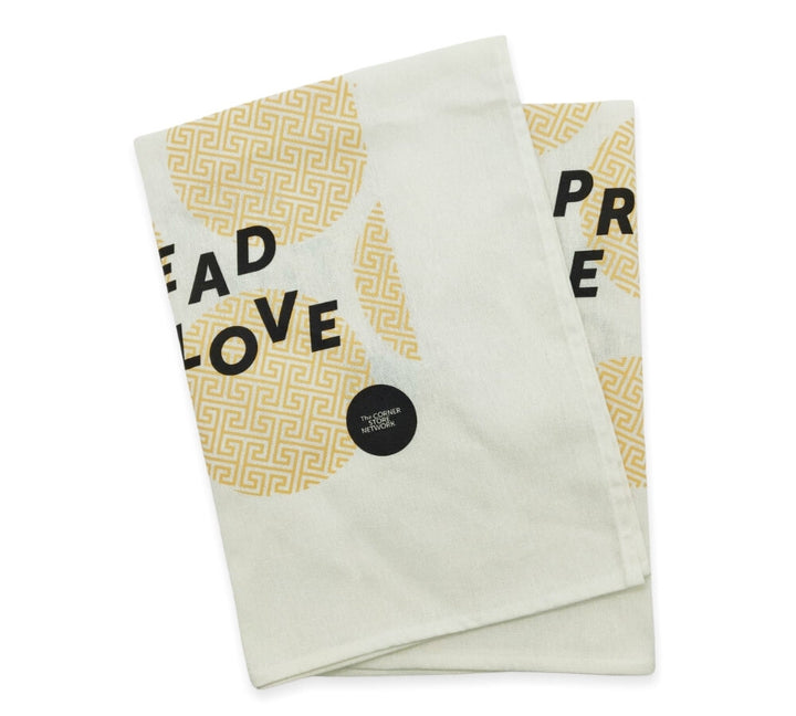 white linen tea towel folded, featuring yellow and white patterned circles with the words spread the love scattered throughout